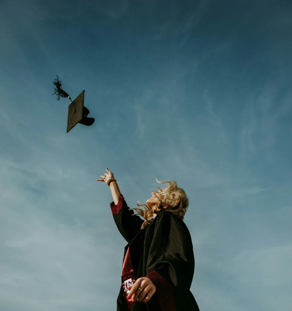 A graduating woman joyfully throwing her graduation cap into the air.