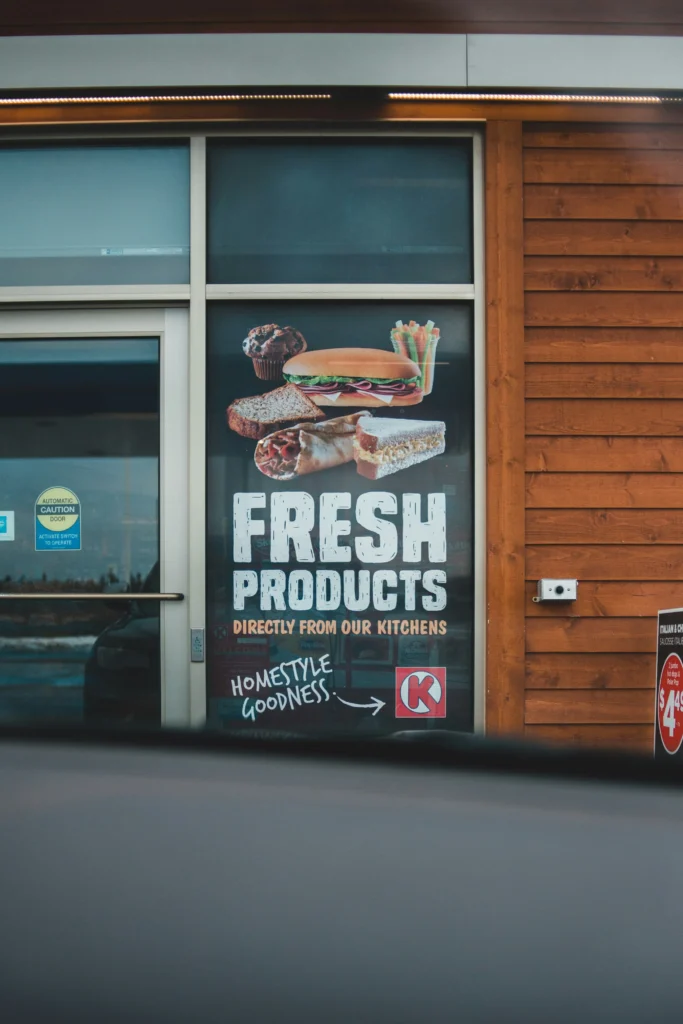 Restaurant window sign featuring printed images of a burger, club sandwich, and wrap for food advertising.